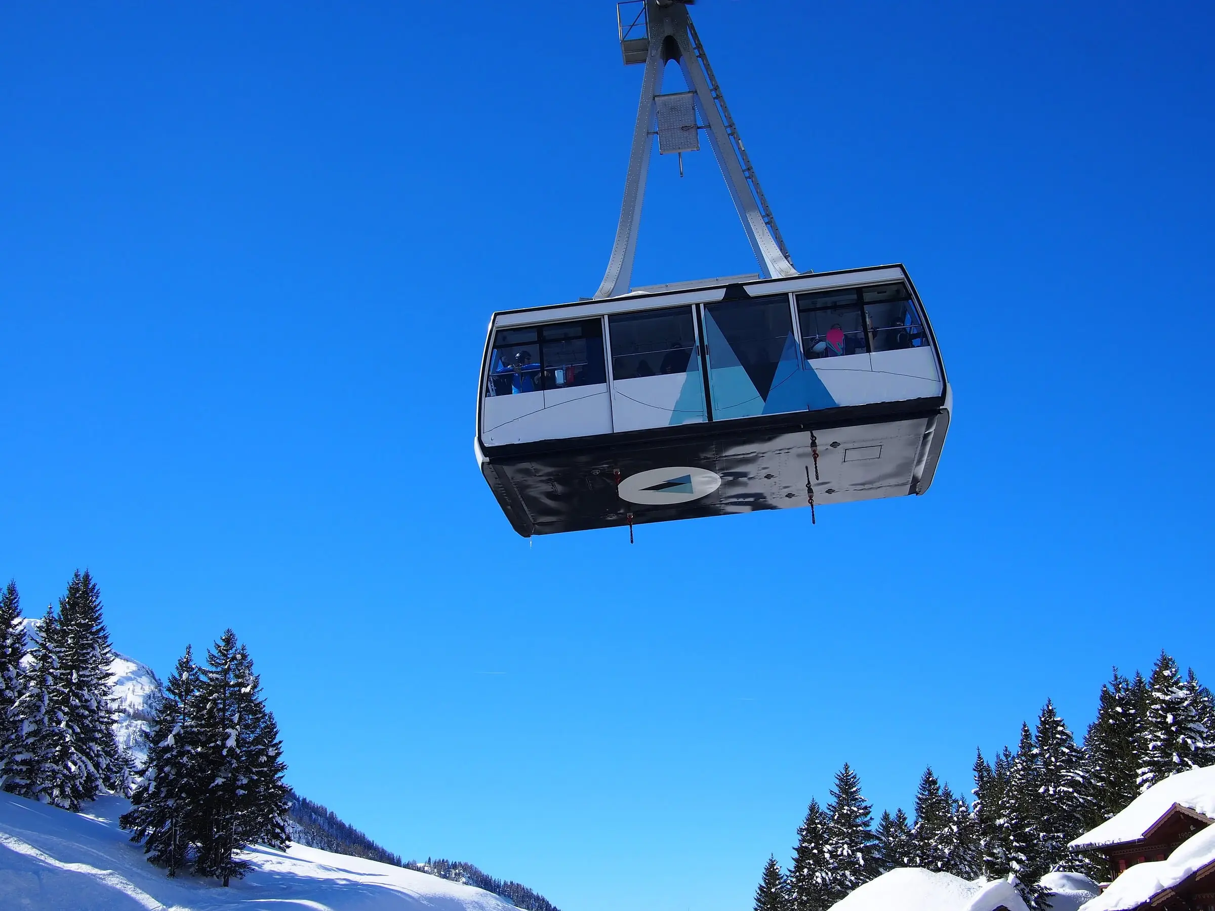 Seilbahnkabine vor tiefblauem Himmel über verschneiten Tannen