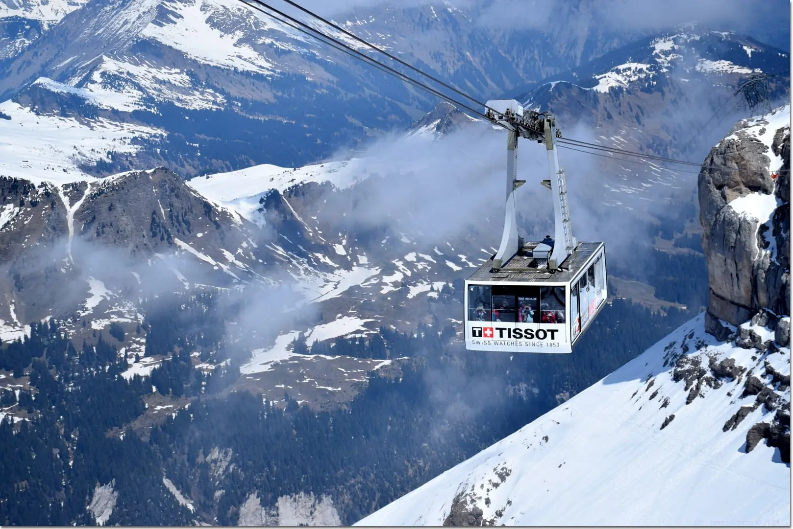Cable car cabin gliding above cloud and snowy cliffs
