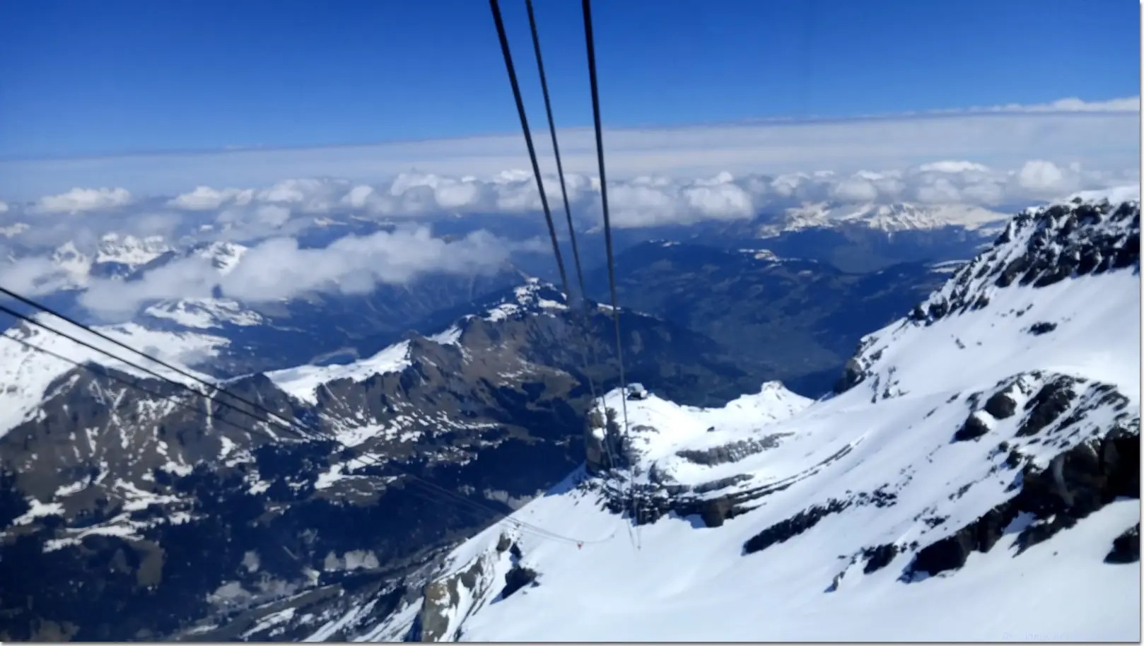 Cable car cables plunging over snowy peaks and clouds