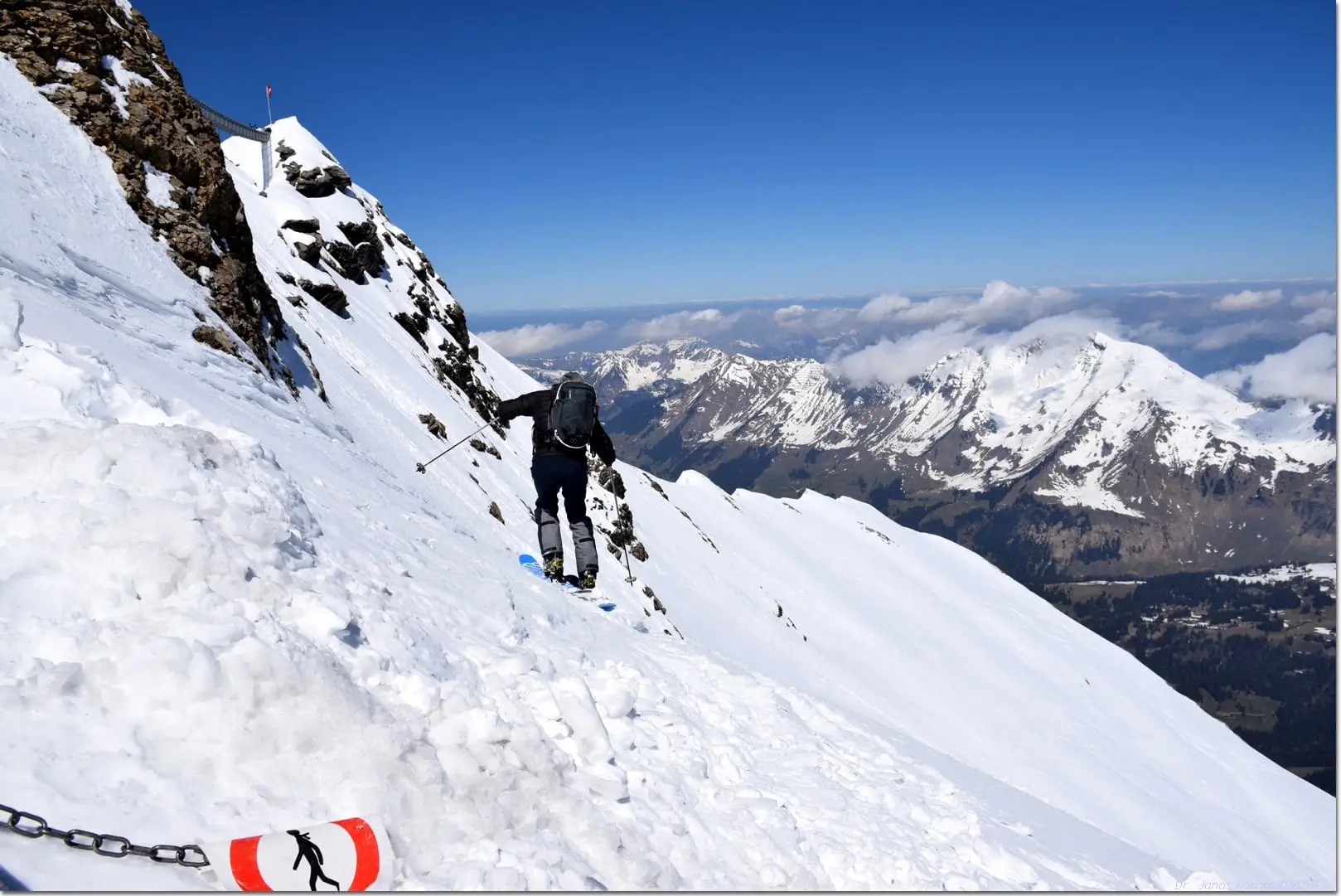 Snowboarder hiking a steep snow ridge above the valley