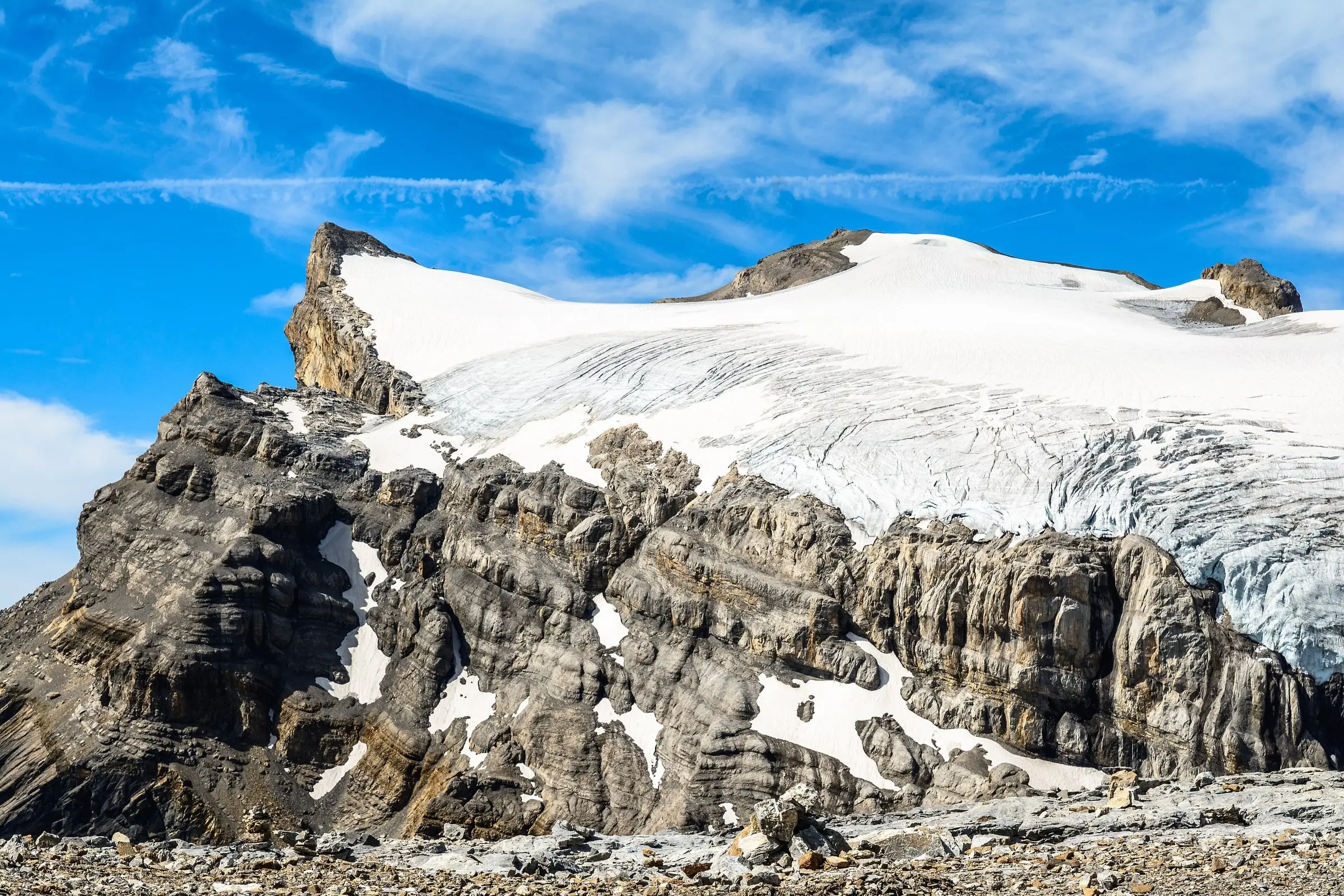 Glacier ice edge spilling over layered limestone cliffs