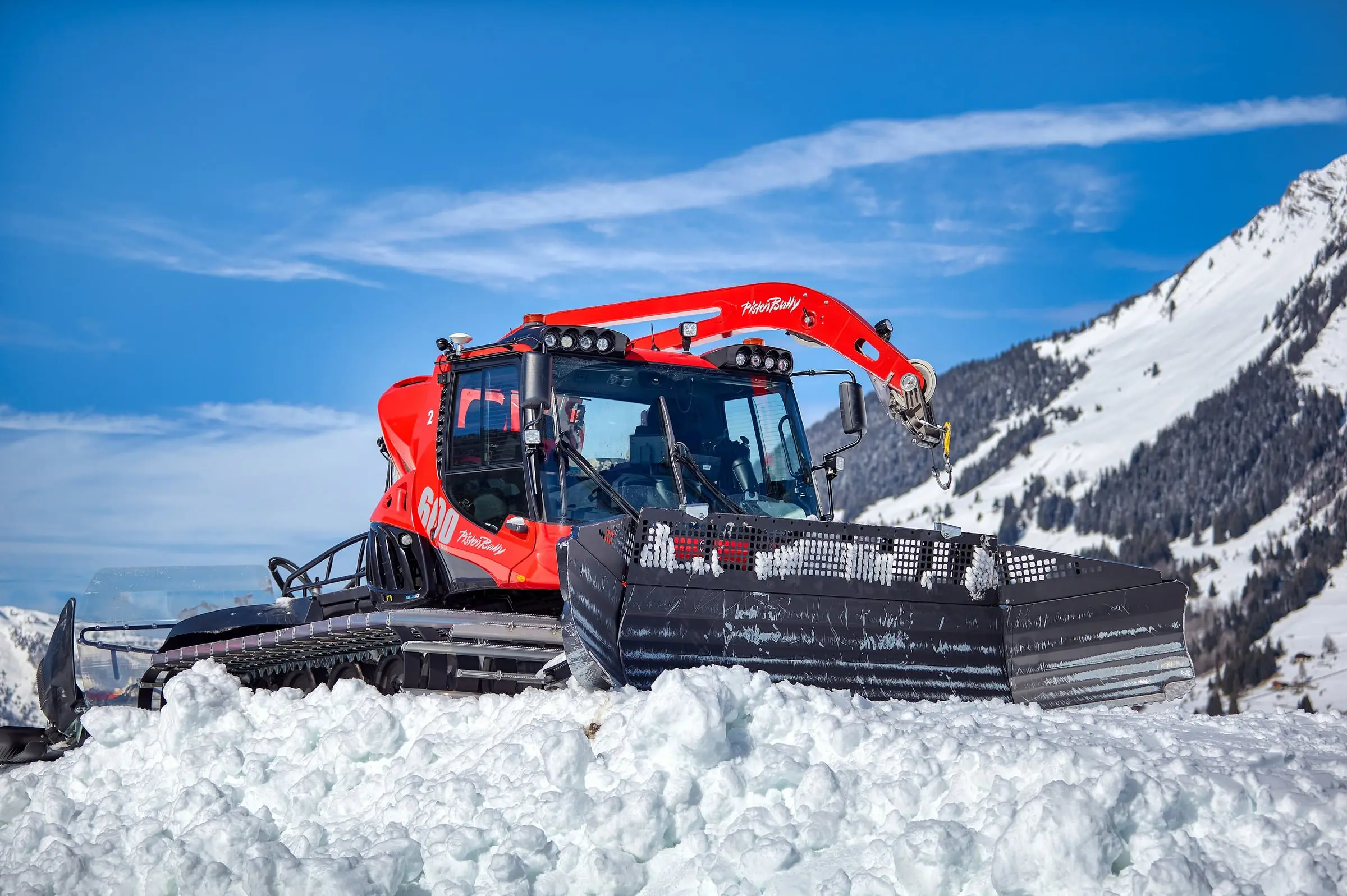 Red piste groomer parked on snow under blue sky