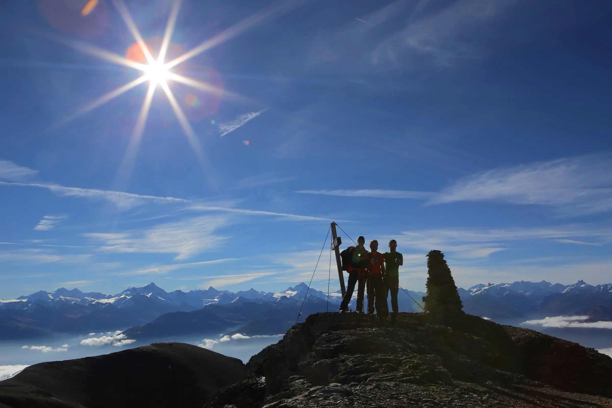 Silhouetten von Wanderern auf dem Gipfel im grellen Gegenlicht